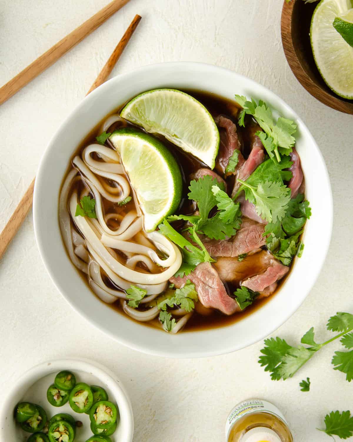A bowl of beef pho completed and topped with limes and cilantro.