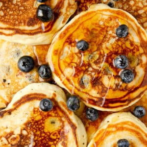 Overhead view of blueberry pancakes topped with fresh blueberries and maple syrup.