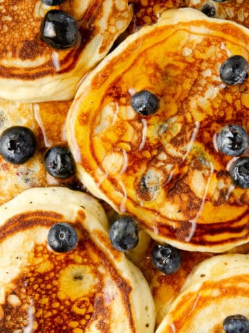 Overhead view of blueberry pancakes topped with fresh blueberries and maple syrup.
