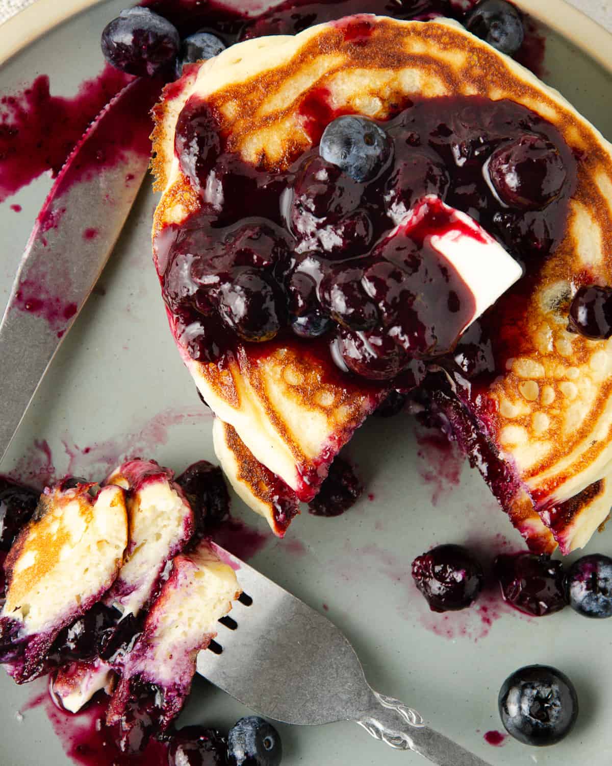 A close up of a stack of pancakes topped with blueberry compote and fresh blueberries.
