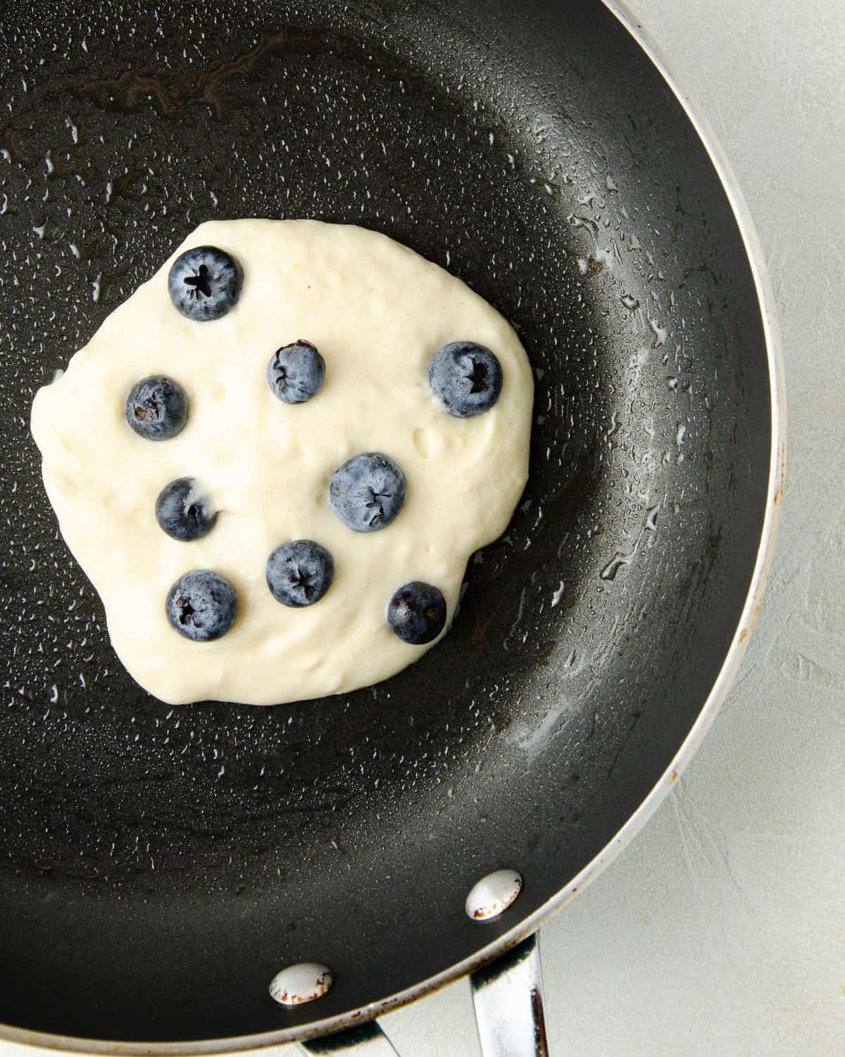 The pancake batter on a pan with blueberries added after.