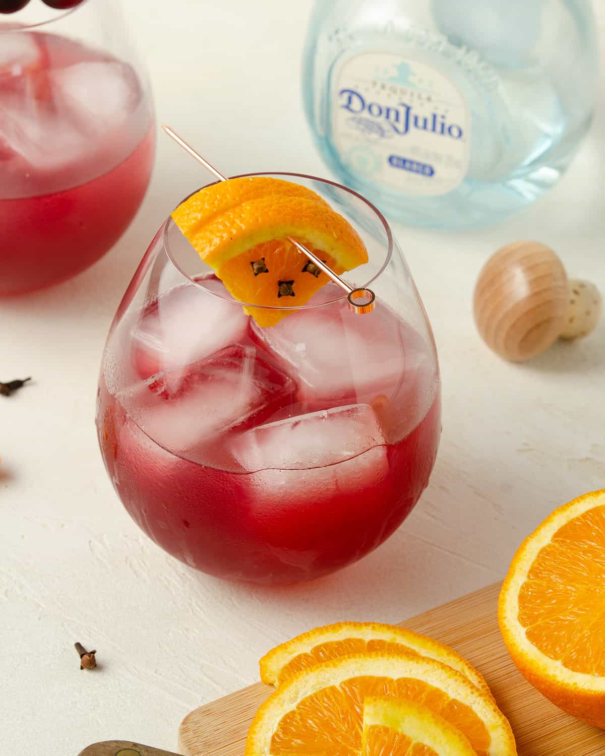 A cranberry margarita with a cutting board of oranges and a bottle of tequila in back.