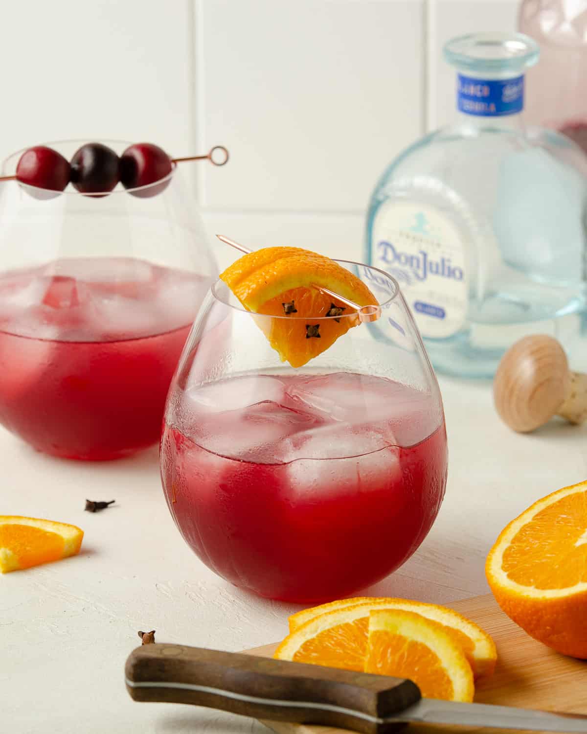 Two glasses of skinny cranberry margarita with a cutting board of fresh oranges.