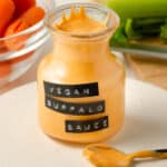 Angled view of a jar of vegan buffalo sauce with some sauce on a spoon.