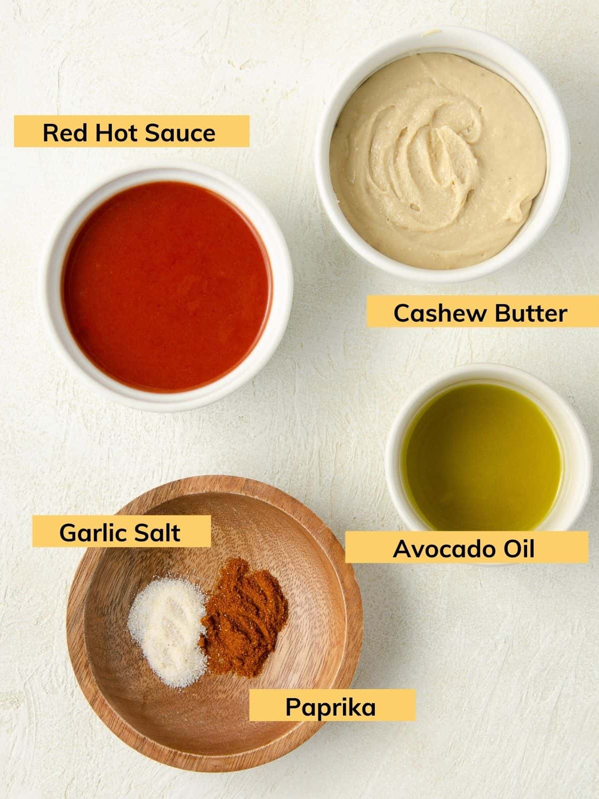 Ingredients for making vegan buffalo sauce: cashew butter, avocado oil, red hot sauce, garlic salt and paprika.