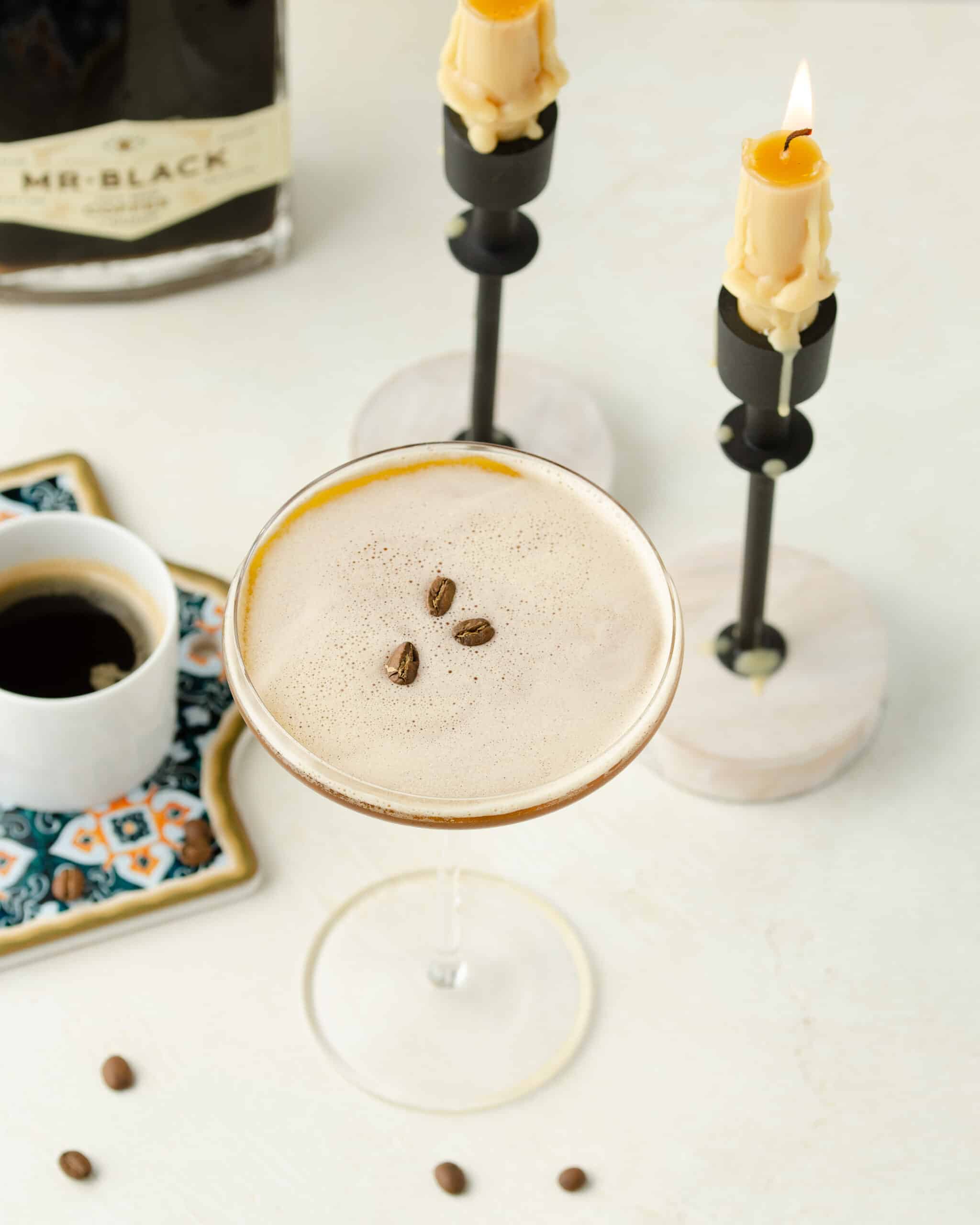 Espresso martini in a glass on the counter with candles burning and cup of espresso.