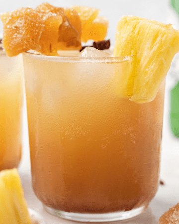 a frosty glass with pineapple ginger beer mocktail topped with candied ginger, fresh pineapple, and star anise