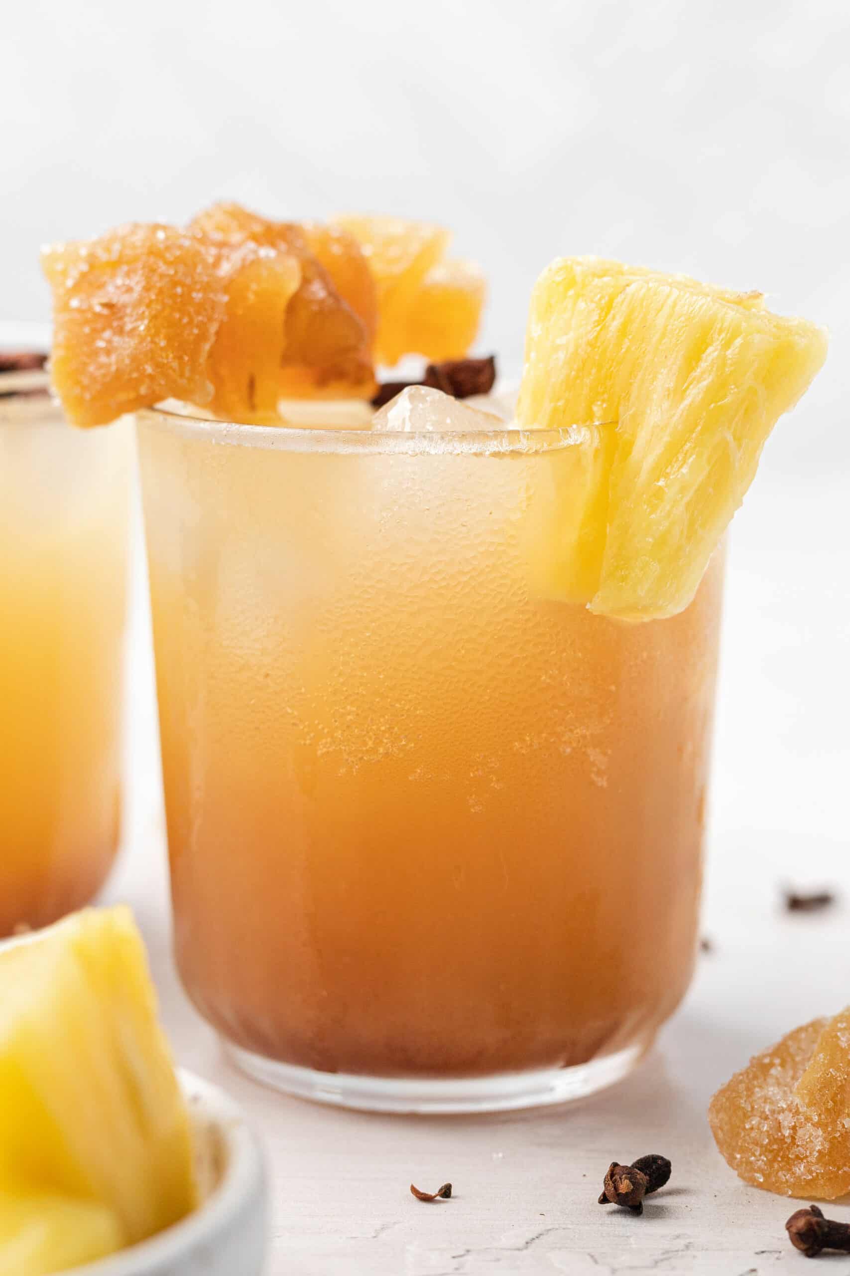 a frosty glass with pineapple ginger beer mocktail topped with candied ginger and fresh pineapple