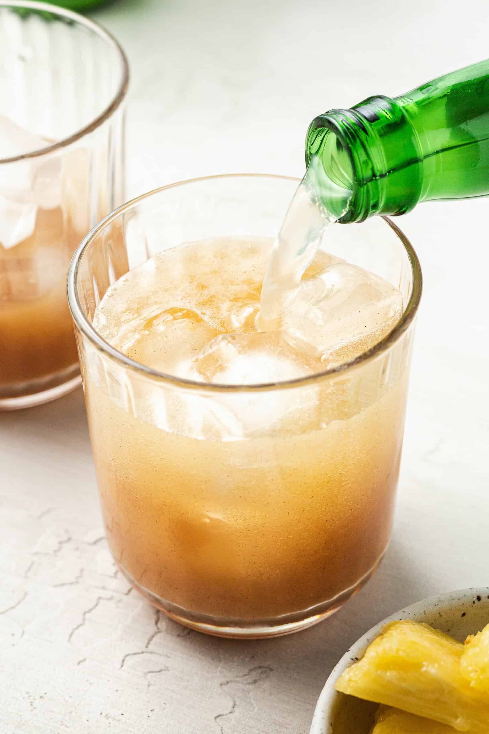 pouring ginger beer into a glass with spicy pineapple syrup
