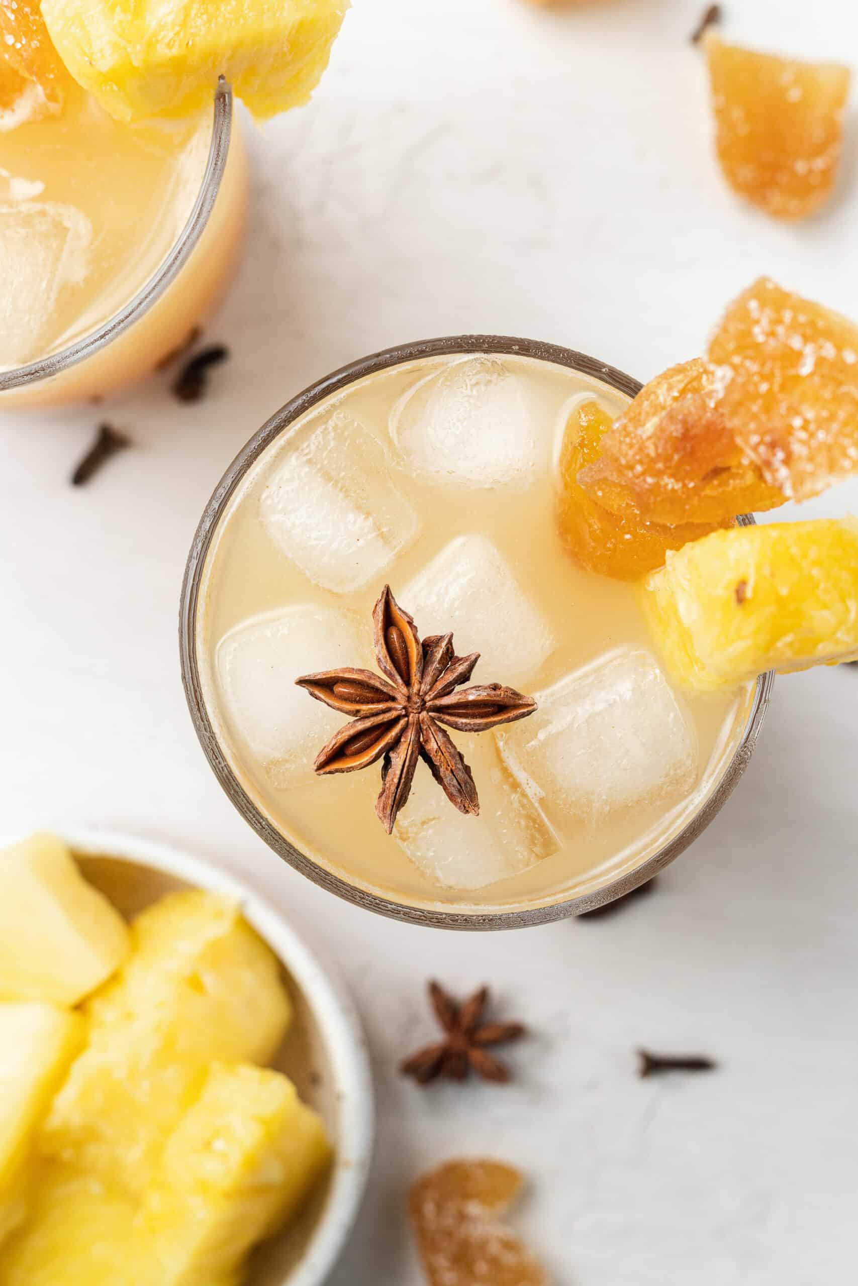 overhead shot of a glass with pineapple ginger beer mocktail topped with candied ginger, fresh pineapple, and star anise