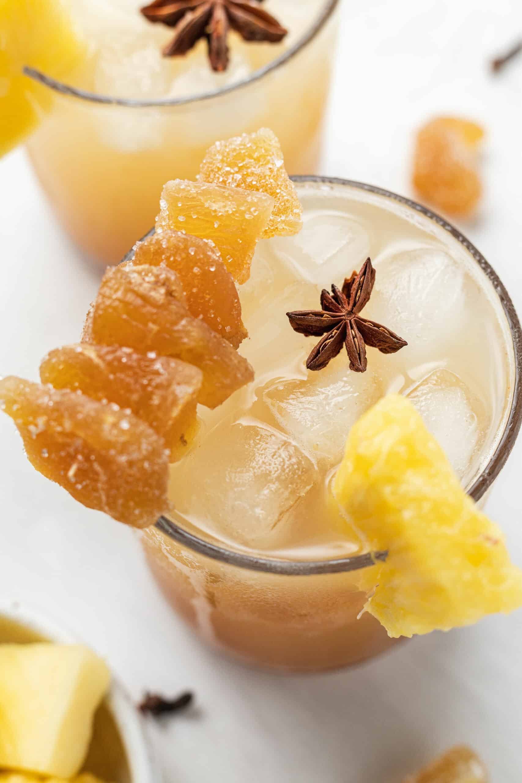 a glass with pineapple ginger beer mocktail topped with candied ginger, fresh pineapple, and star anise