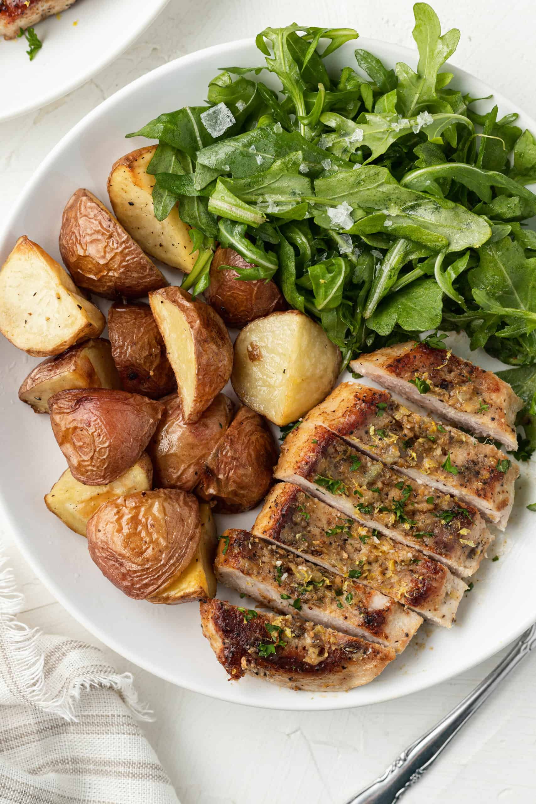 A white plate with sliced pork chops served with roasted potatoes and salad.