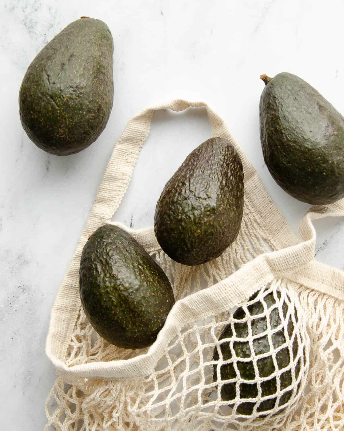A white mesh bag with 5 avocados spilling out onto the counter. 