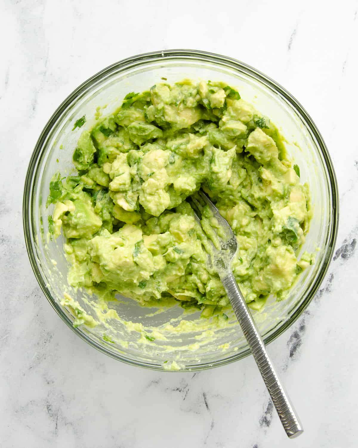 Mashed guacamole in a glass bowl on a white counter top. 