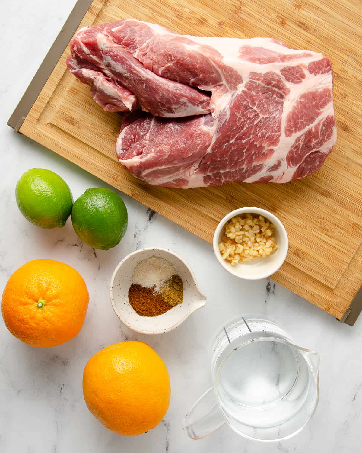 Ingredients needed for dutch oven carnitas: pork shoulder, oranges, limes, water, seasonings, and garlic. 