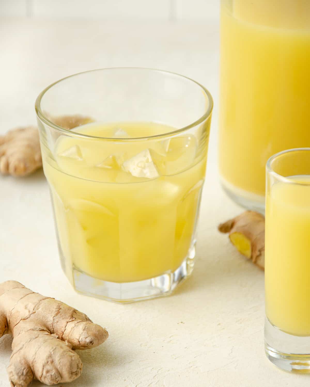 A glass of ginger juice with ice and. More ginger juice and fresh ginger in the background.