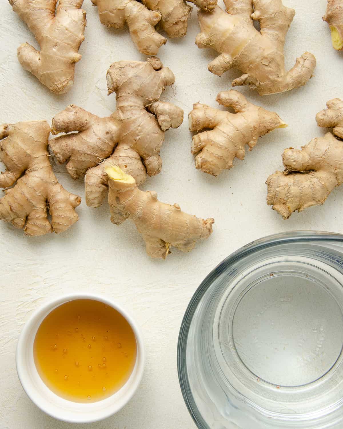 Pieces of fresh ginger root on a white counter with honey and water in glass containers.