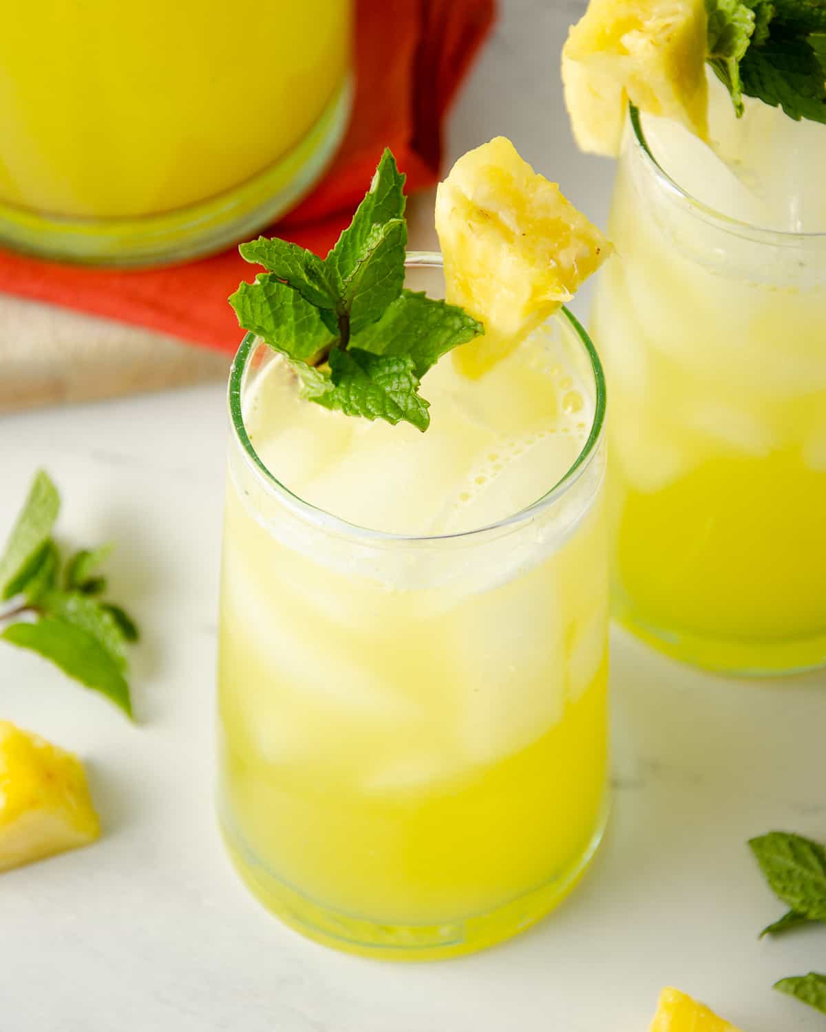 Two glasses of pineapple water with a pitcher.