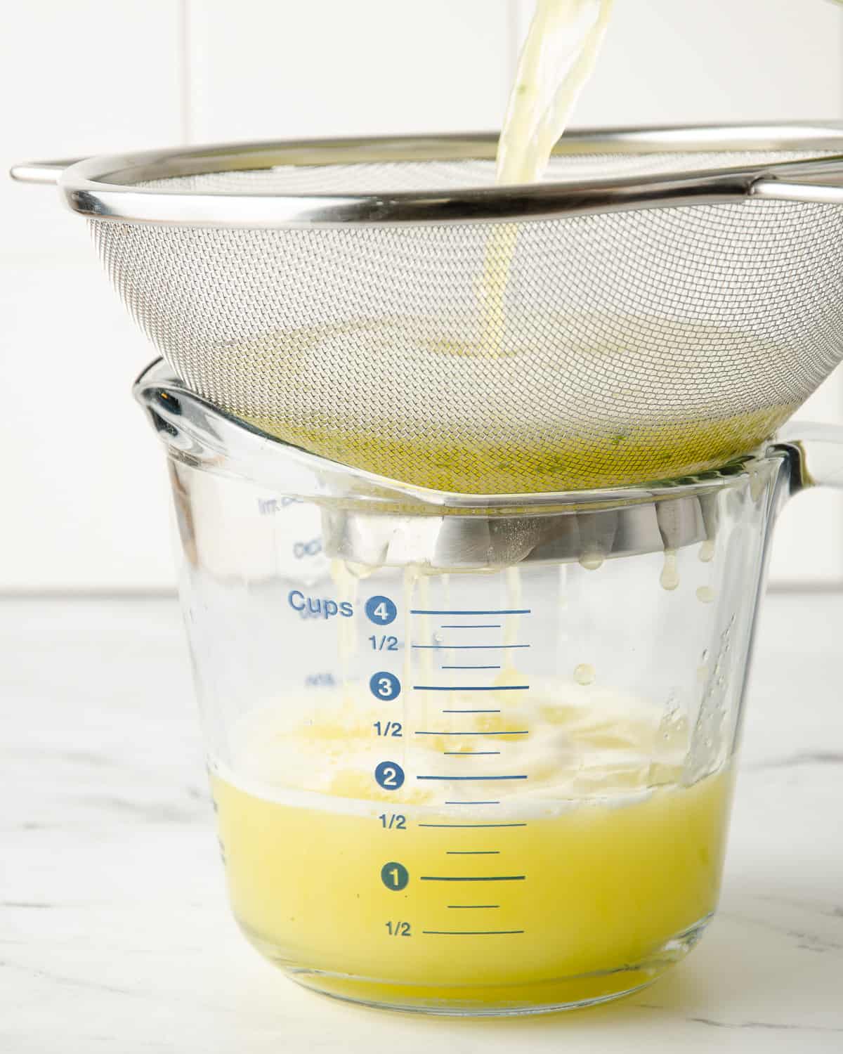Straining pineapple water through a sieve into a large measuring cup.