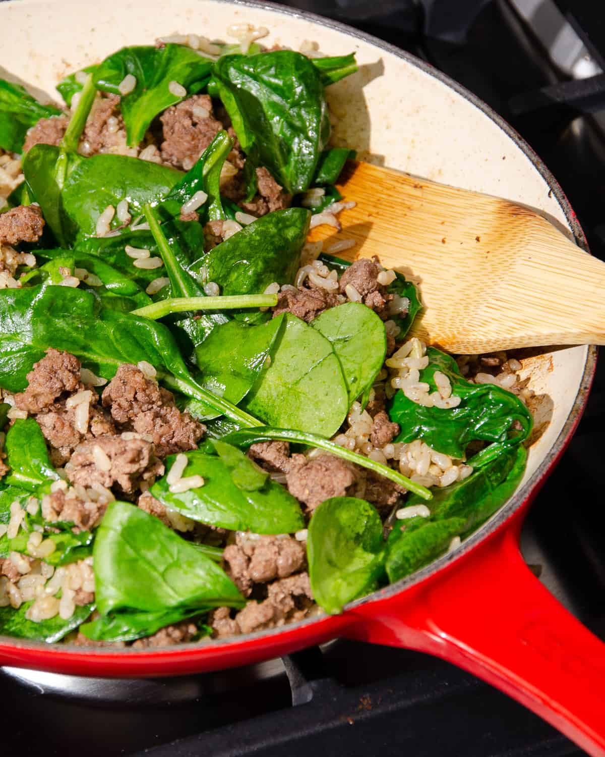 Browned ground beef, rice, and spinach in a red skillet.