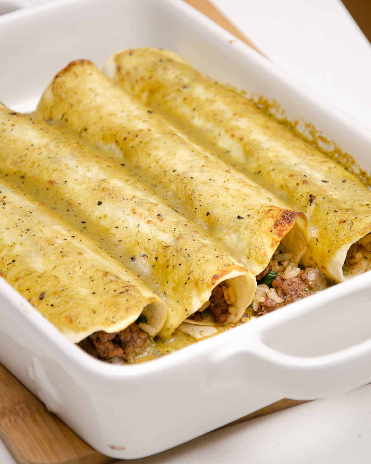 Beef enchiladas with green sauce in a white casserole dish.