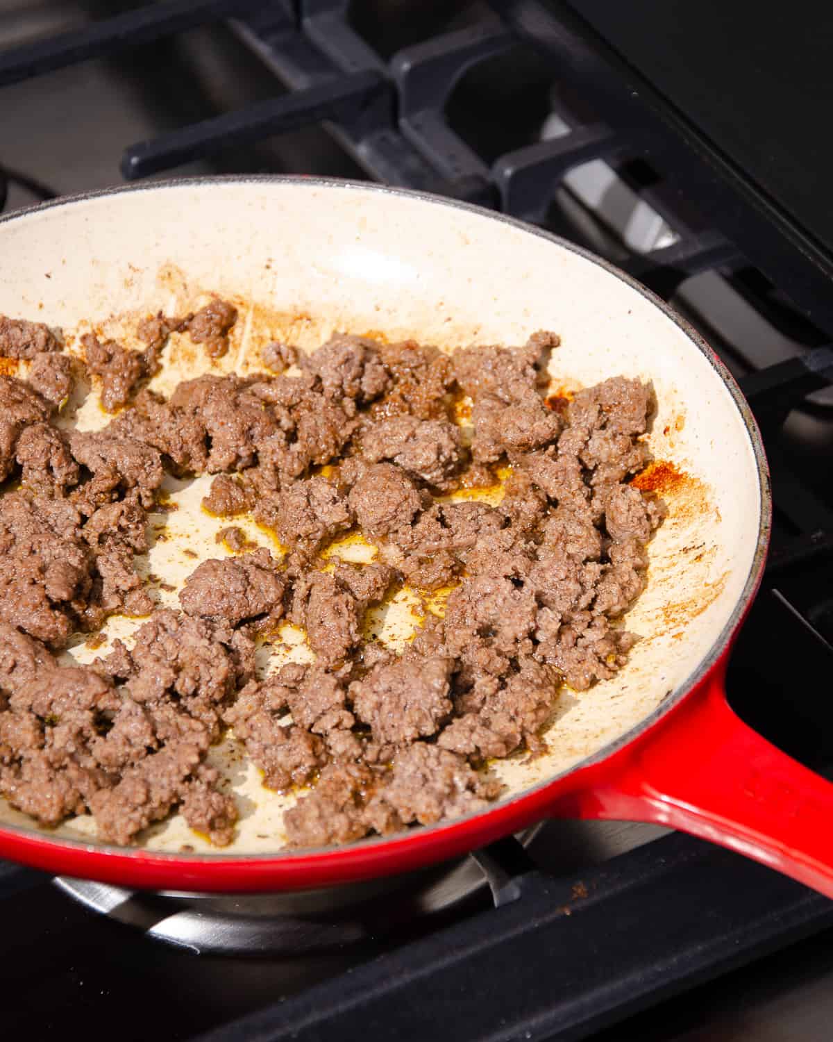 Browned ground beef in a red skillet.