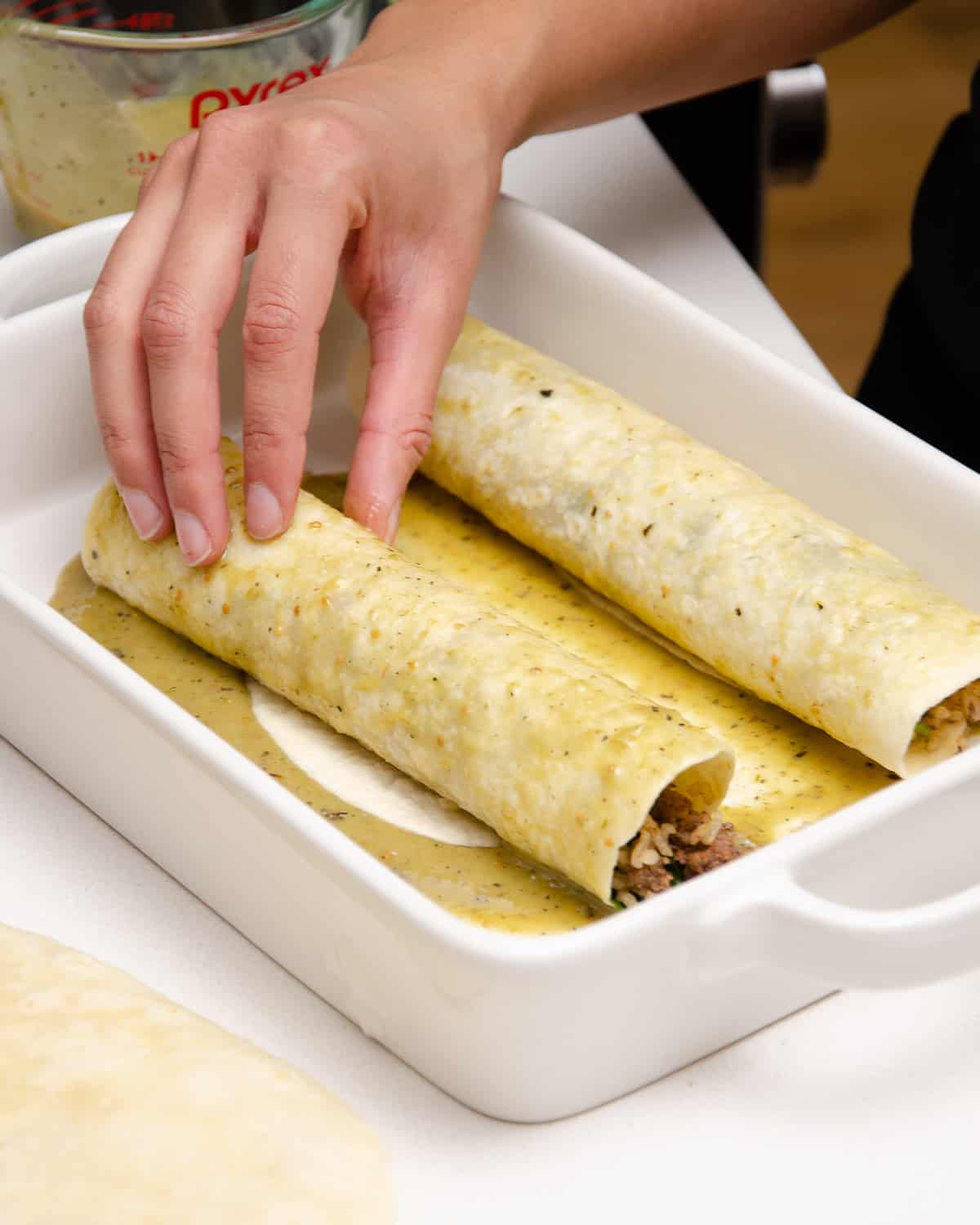 Two rolled beef enchiladas in a white casserole dish with green chili sauce.