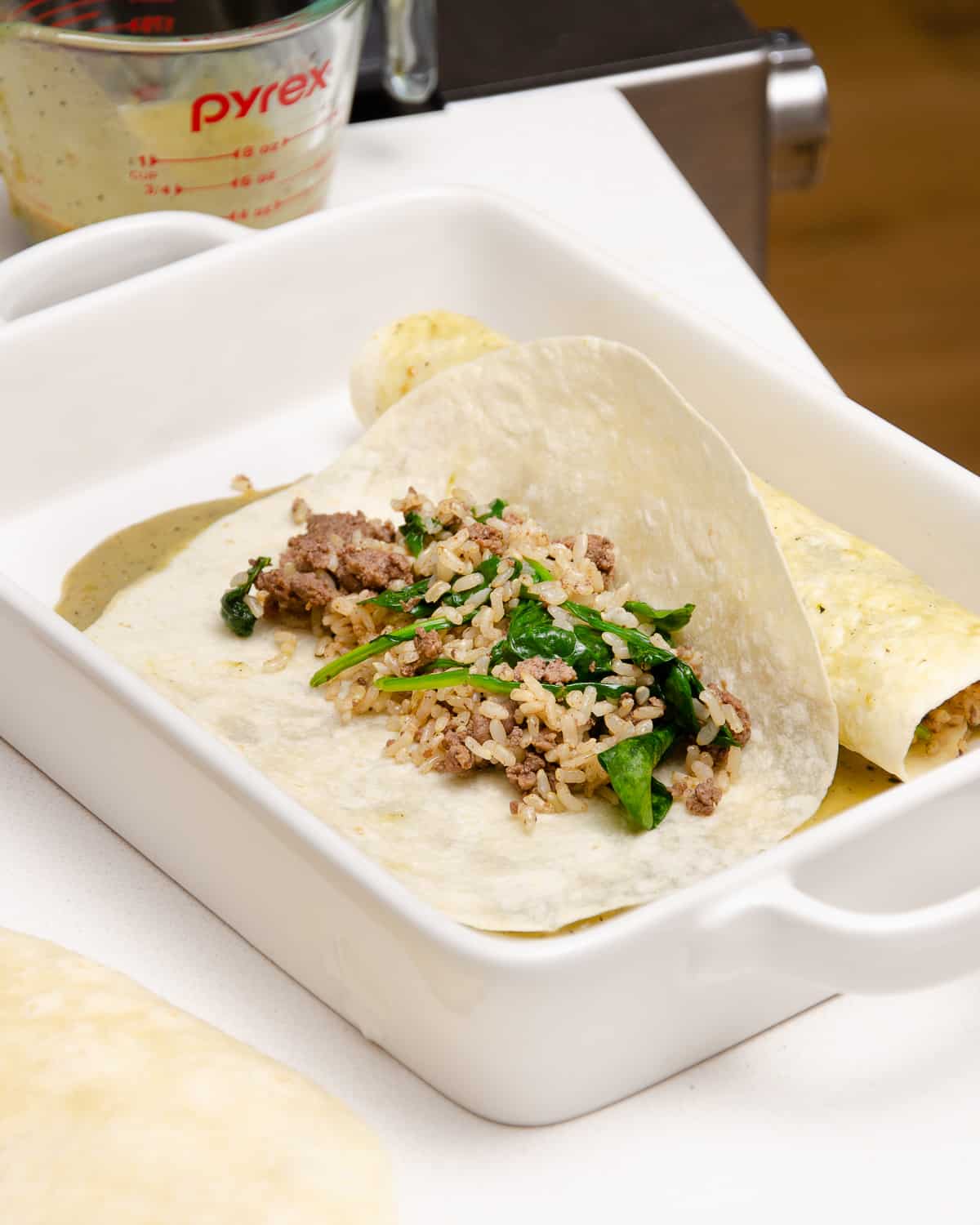 A tortilla filled with rice, ground beef, and spinach in a casserole baking dish.