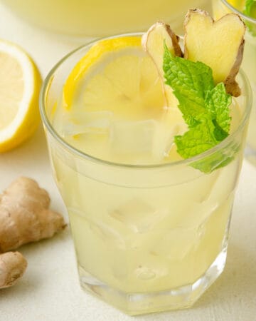 A glass of mint and ginger lemonade topped with fresh lemon slice, ginger, and mint.