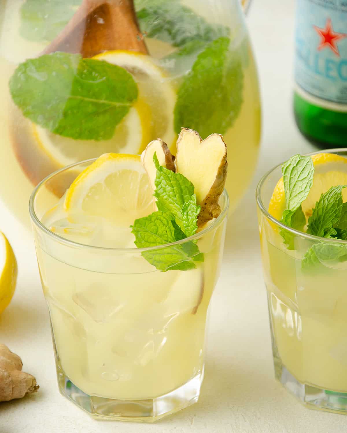 Two glasses of mint and ginger lemonade topped with fresh lemon slice, ginger, and mint.