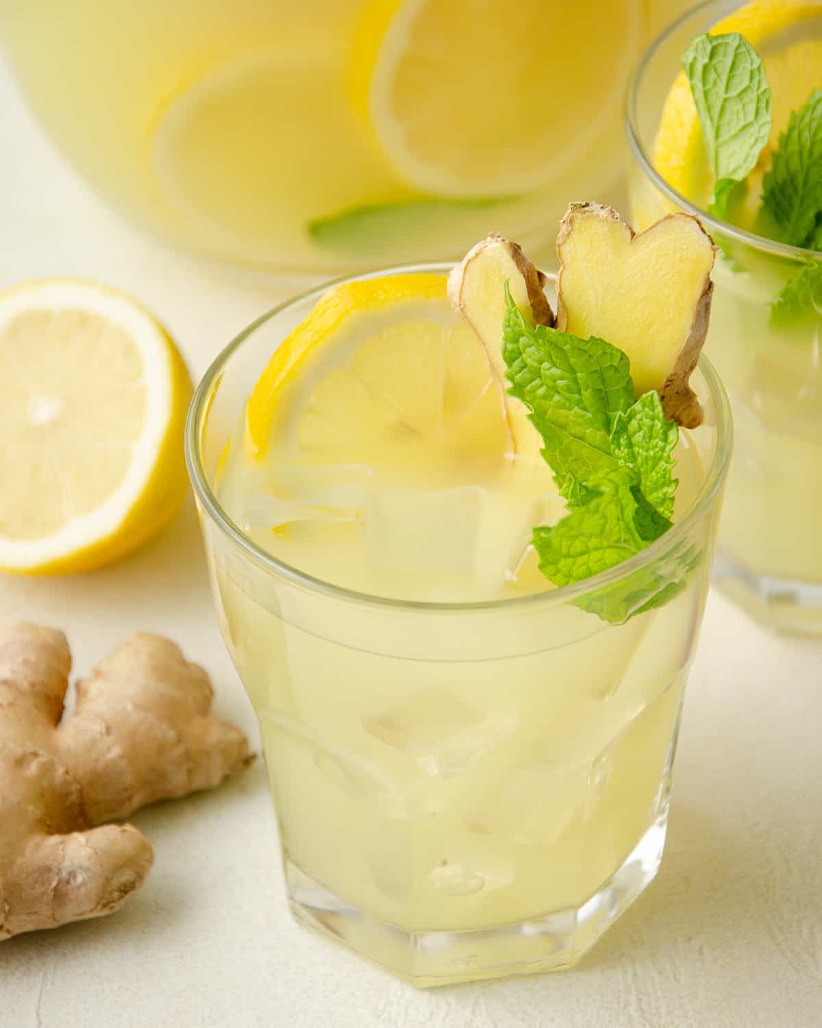 A glass of mint and ginger lemonade topped with fresh lemon slice, ginger, and mint.