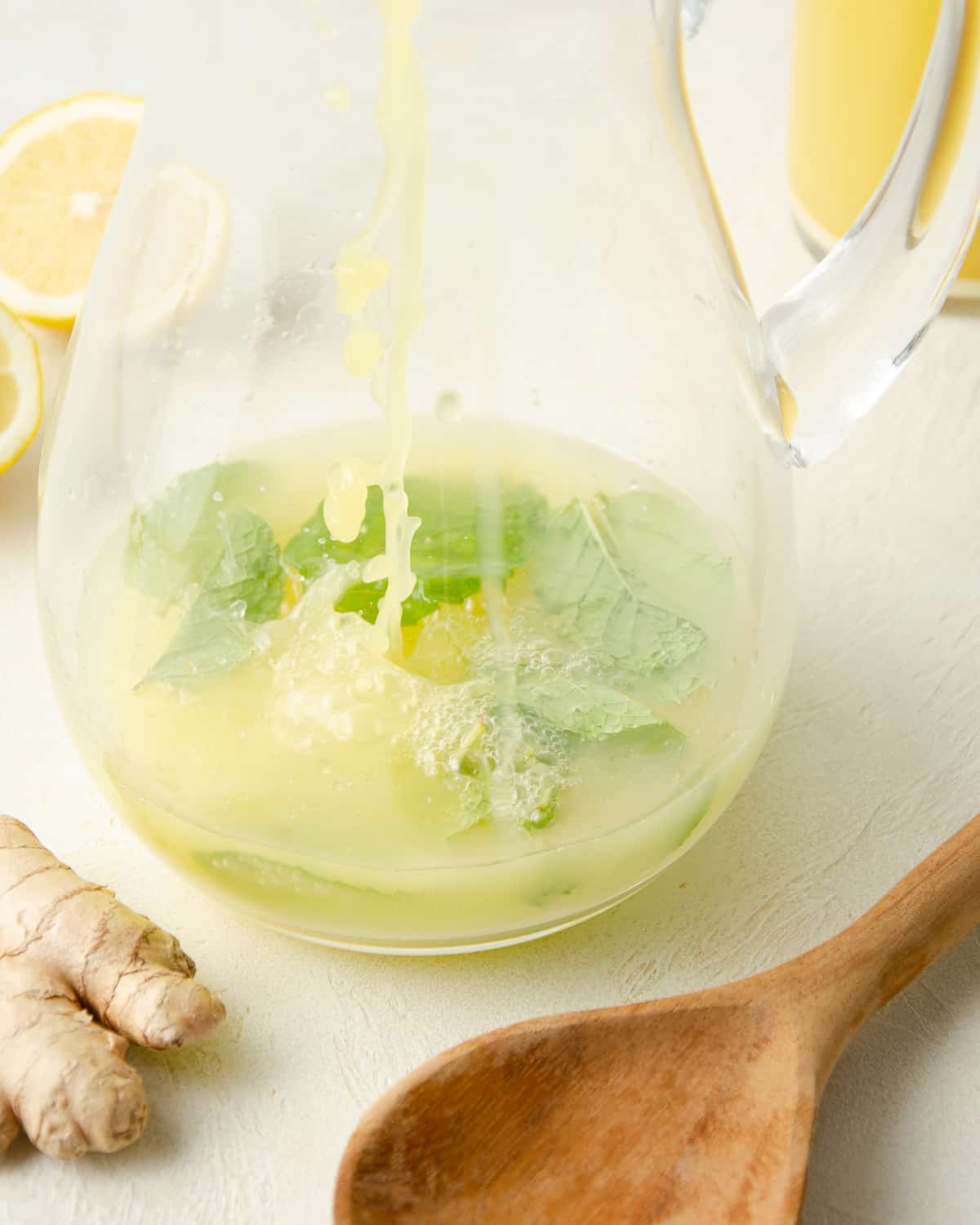 Adding fresh ginger juice to a glass pitcher with mint leaves.