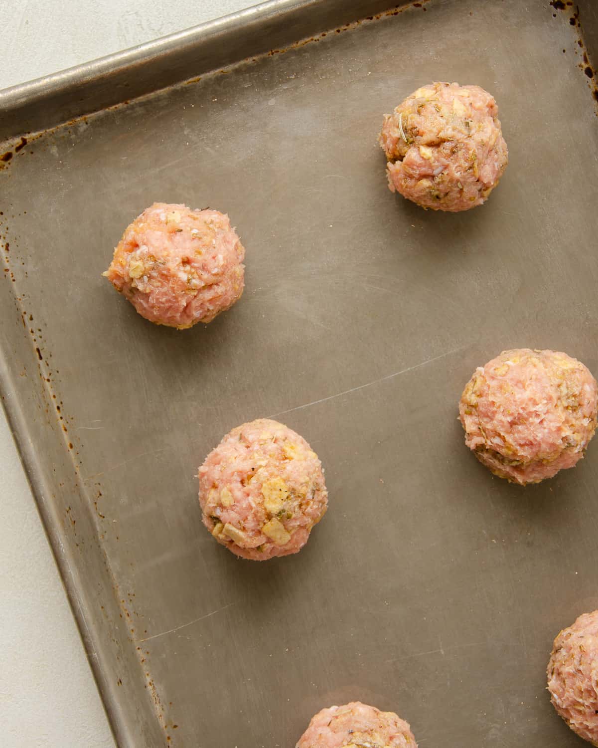 Raw meatballs on a baking sheet ready for the oven.