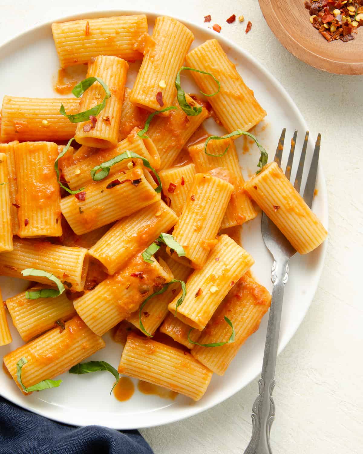 A white plate with rigatoni and dairy free pink pasta sauce, topped with basil and red pepper flakes.