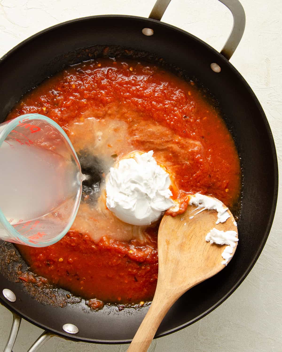 Adding coconut cream and pasta water to a skillet full of marinara sauce.