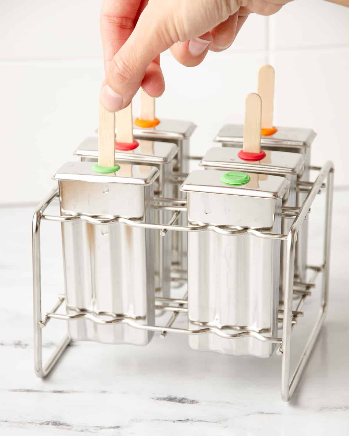A hand putting a popsicle stick into a stainless steel mold.