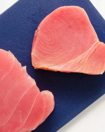 Two pink steaks of ahi tuna sitting atop a blue cutting board.