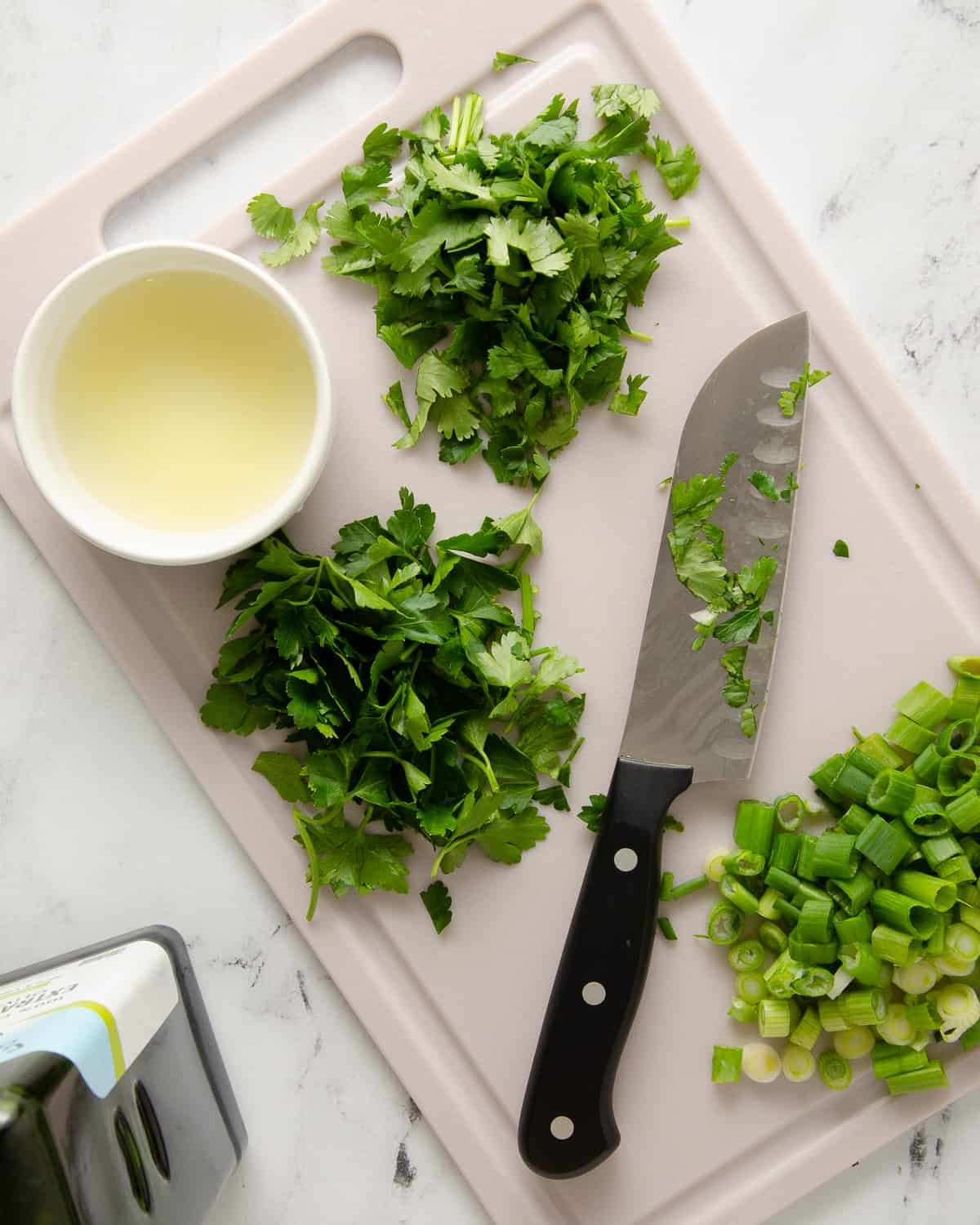 Fresh chopped herbs with a knife on a cutting board on a white counter.