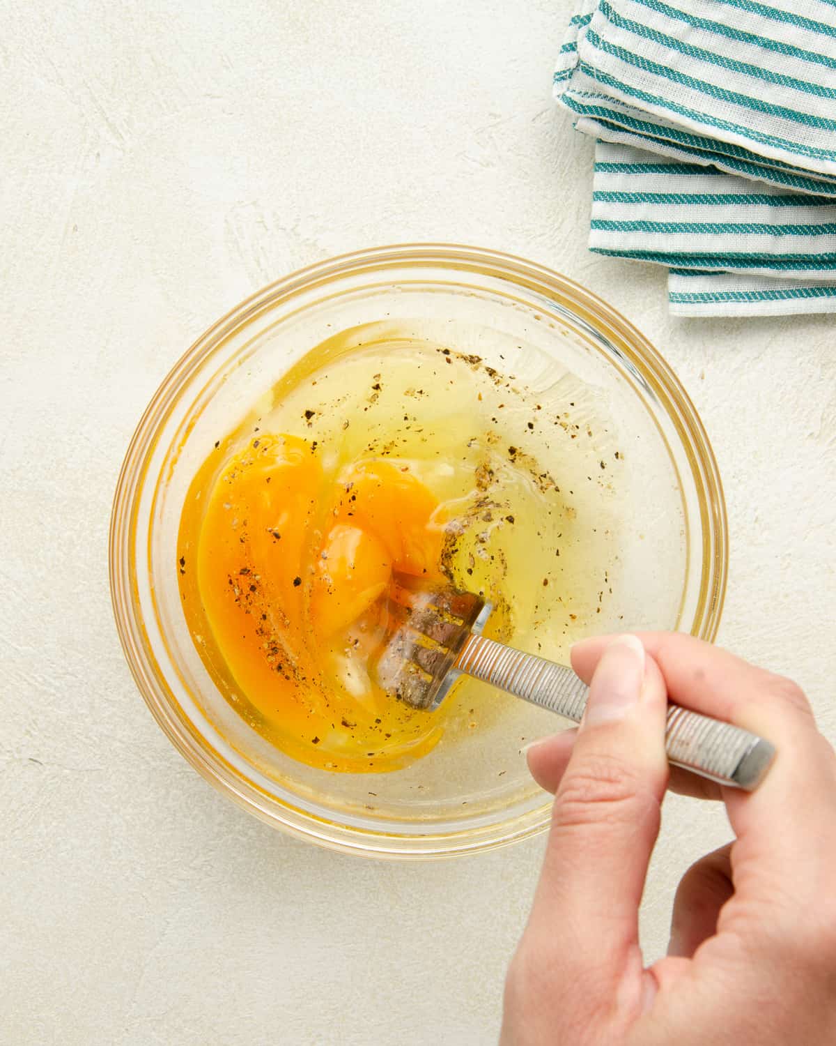 Fork whisking eggs, salt and pepper in a glass bowl.