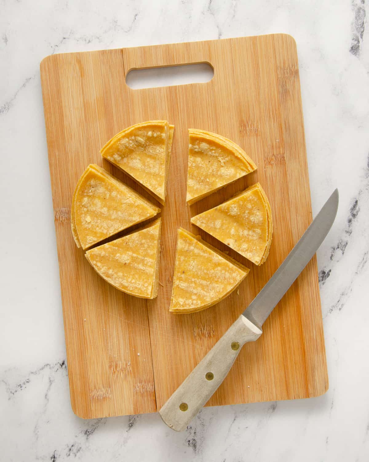 Corn tortillas cut into 6 equal-sized pieces on a cutting board.