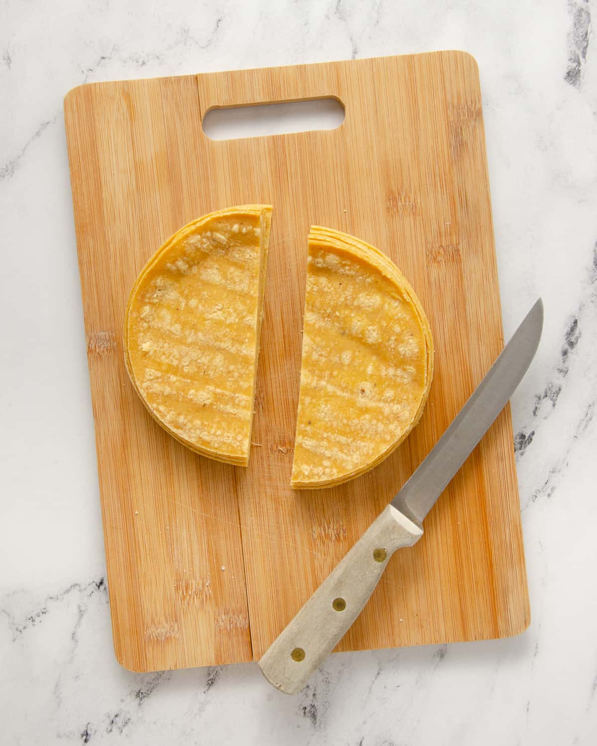Corn tortillas cut in half on a cutting board.
