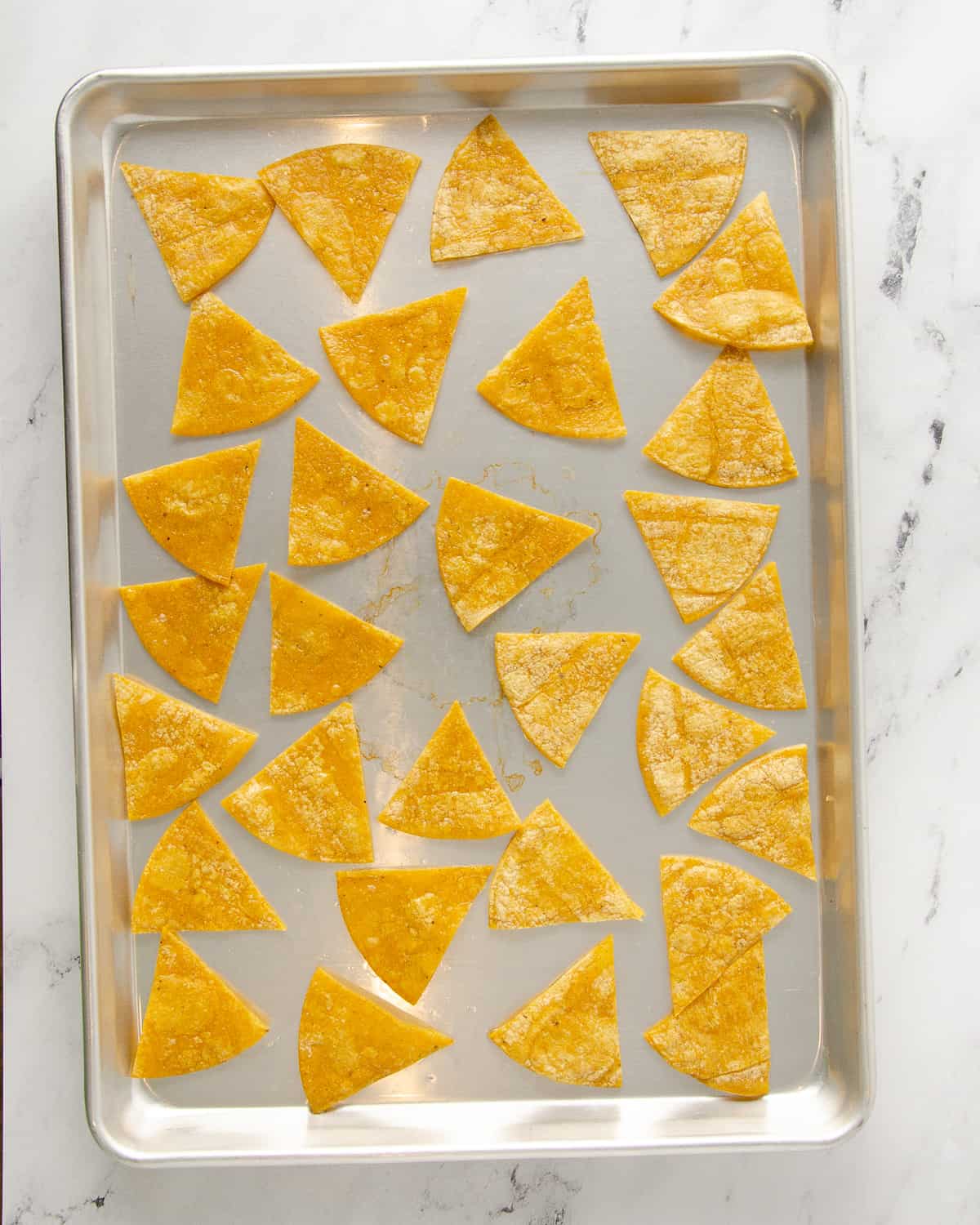Corn tortilla chips lightly browned on both sides on a baking tray.