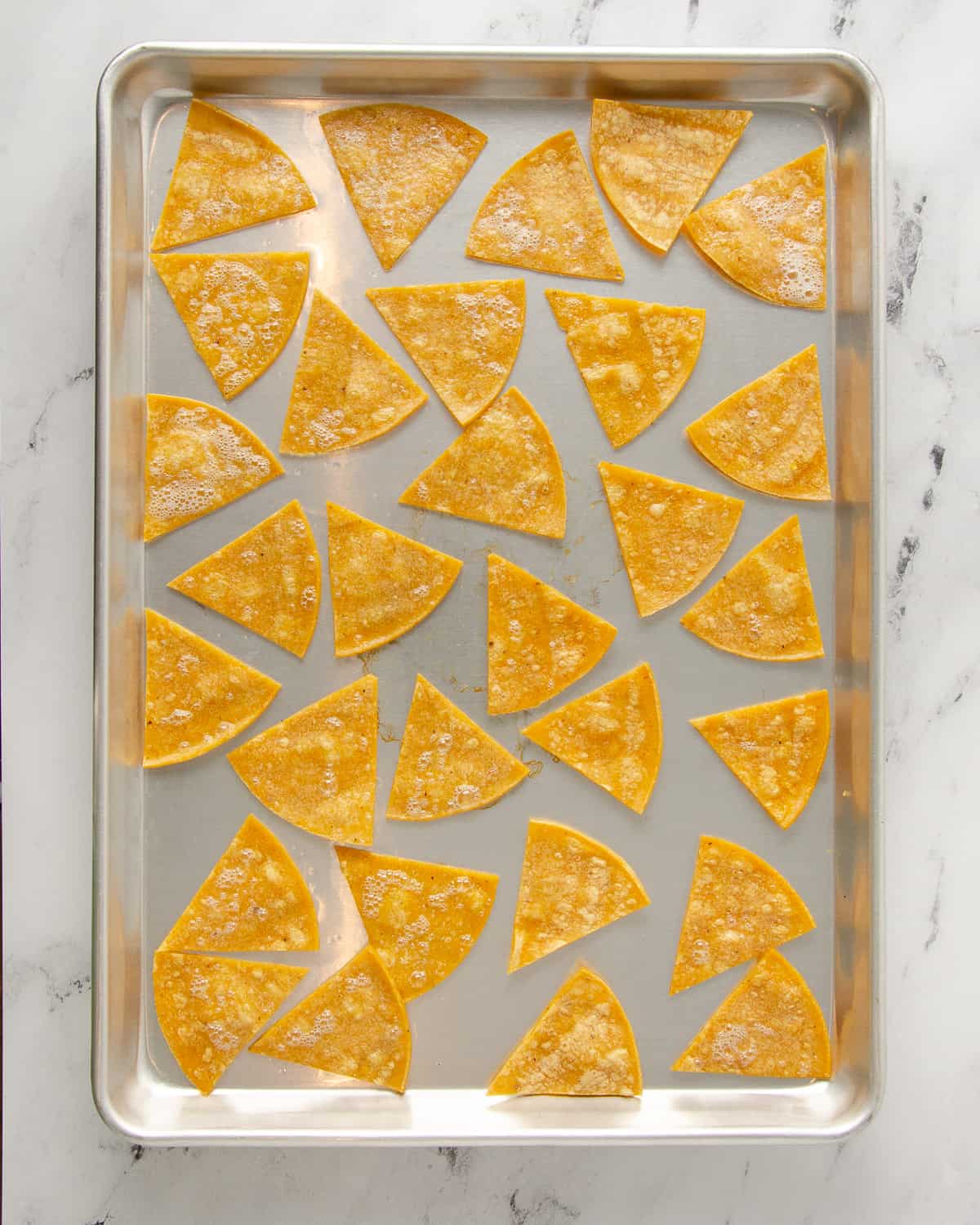 Corn tortilla pieces on a baking tray after being baked on one side and before being flipped.