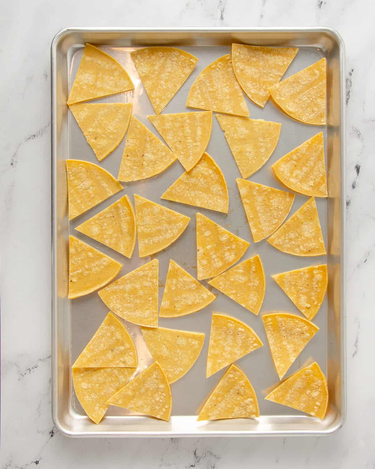 A baking tray with corn tortilla triangles before baking.