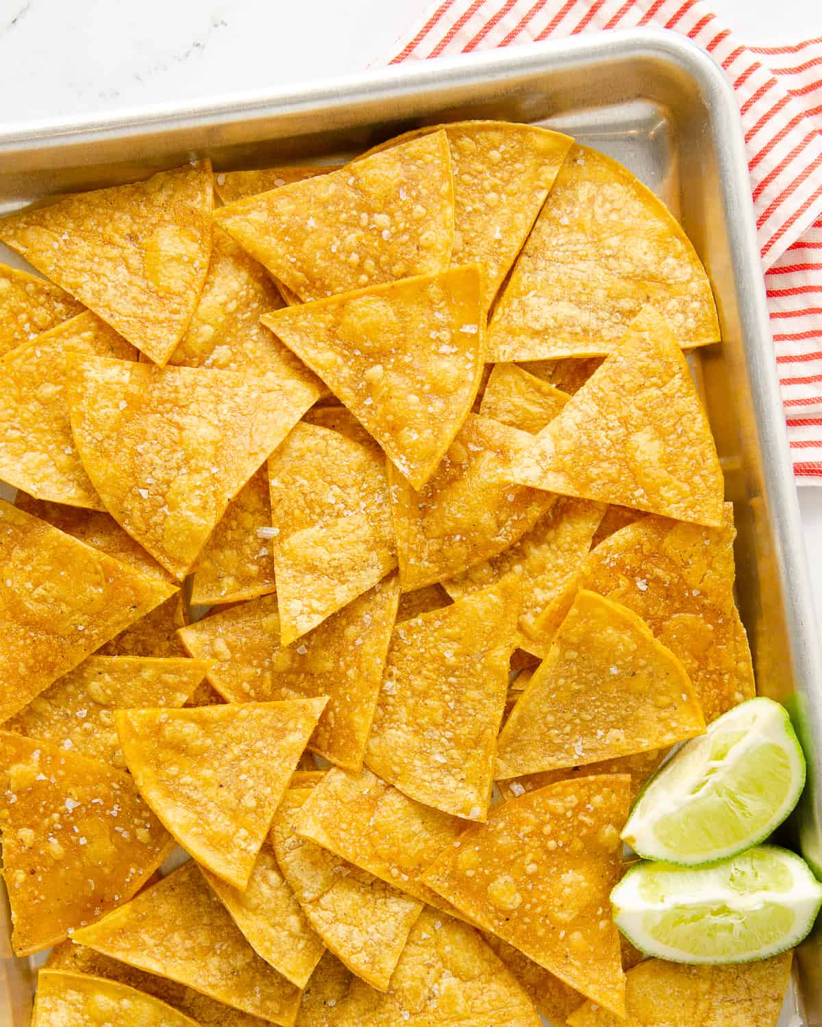 Baked corn tortilla chips on a sheet with limes.
