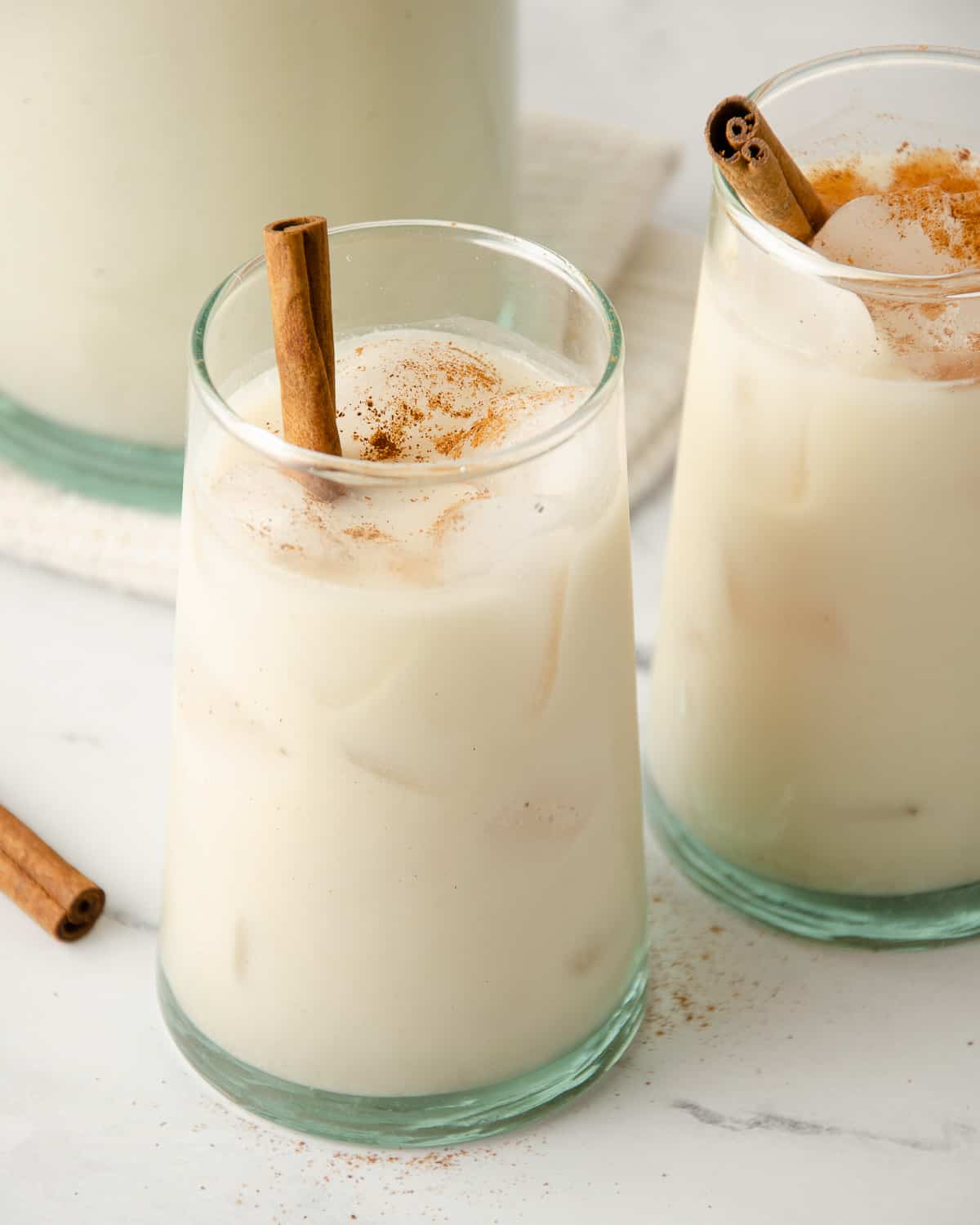 Two glassed of horchata with a cinnamon stick topped with ground cinnamon.