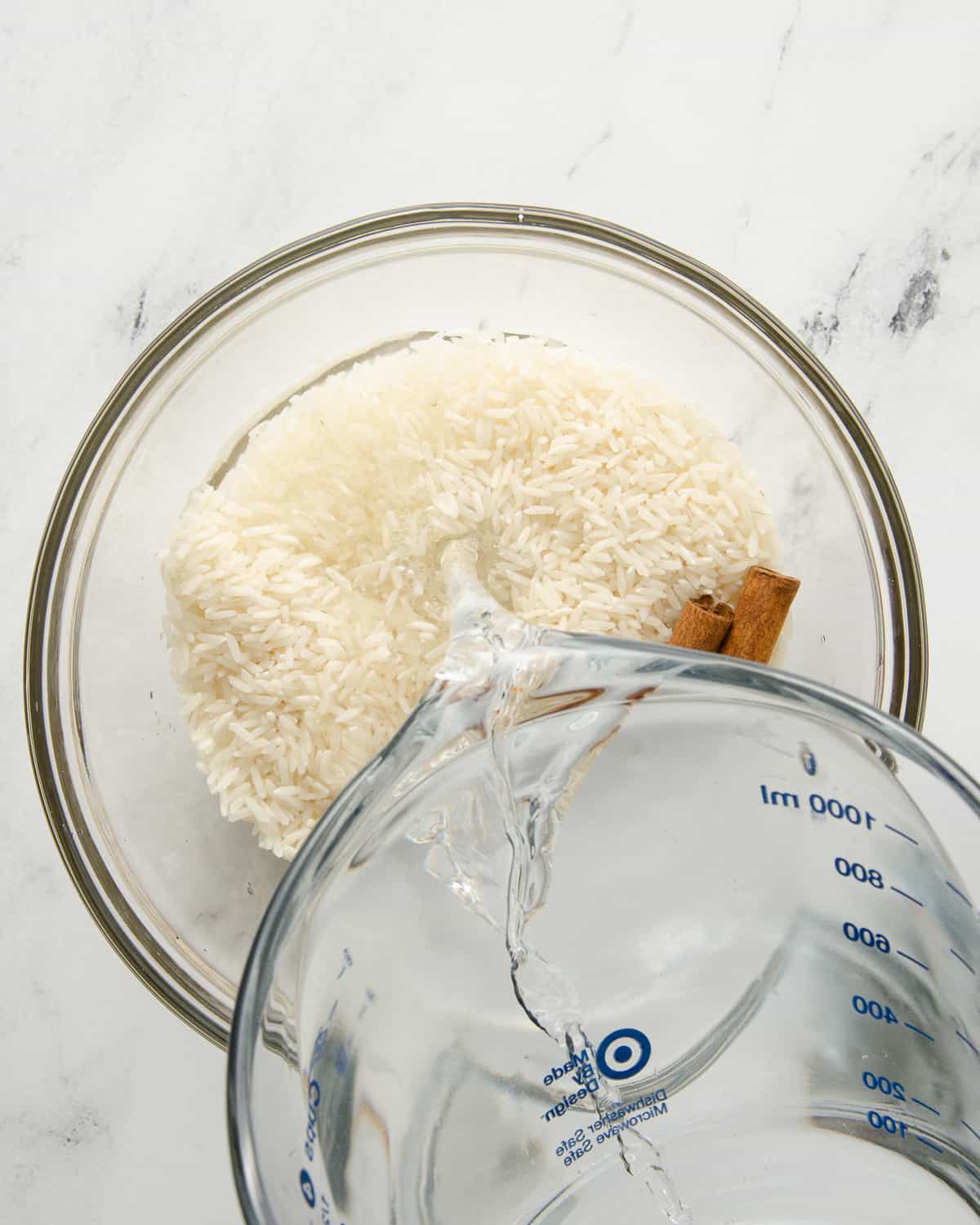 Water being poured into a glass bowl with rice and cinnamon sticks.