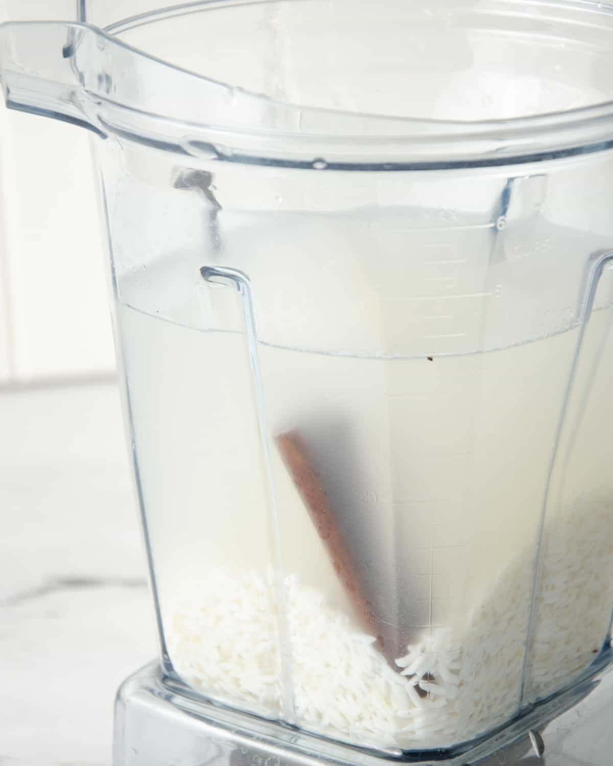 A blender with rice, water, and a cinnamon stick before blending.