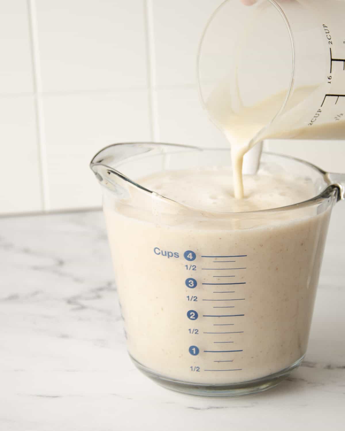 Pouring milk into blended horchata in a glass measuring cup.