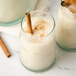 A glass of horchata with a cinnamon stick topped with ground cinnamon.